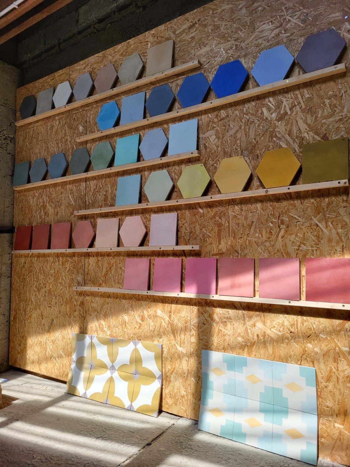 Mur de l'atelier : rangées de carreaux unis classés par teintes, des gris et bleus aux verts, jaunes, rouges et roses