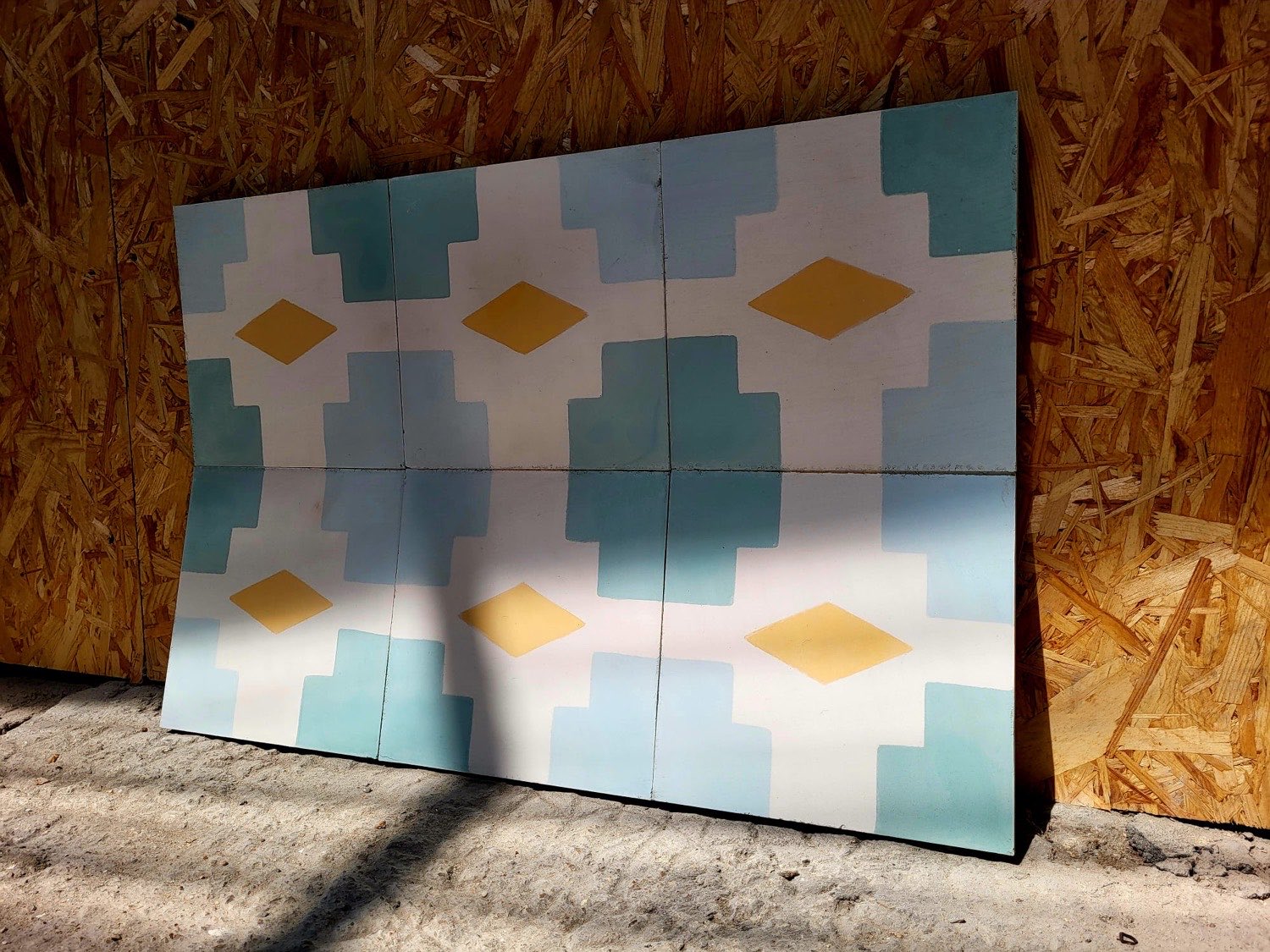 Panneau de carreaux bleus, verts et ocre adossé au mur en panneaux de bois de l'atelier