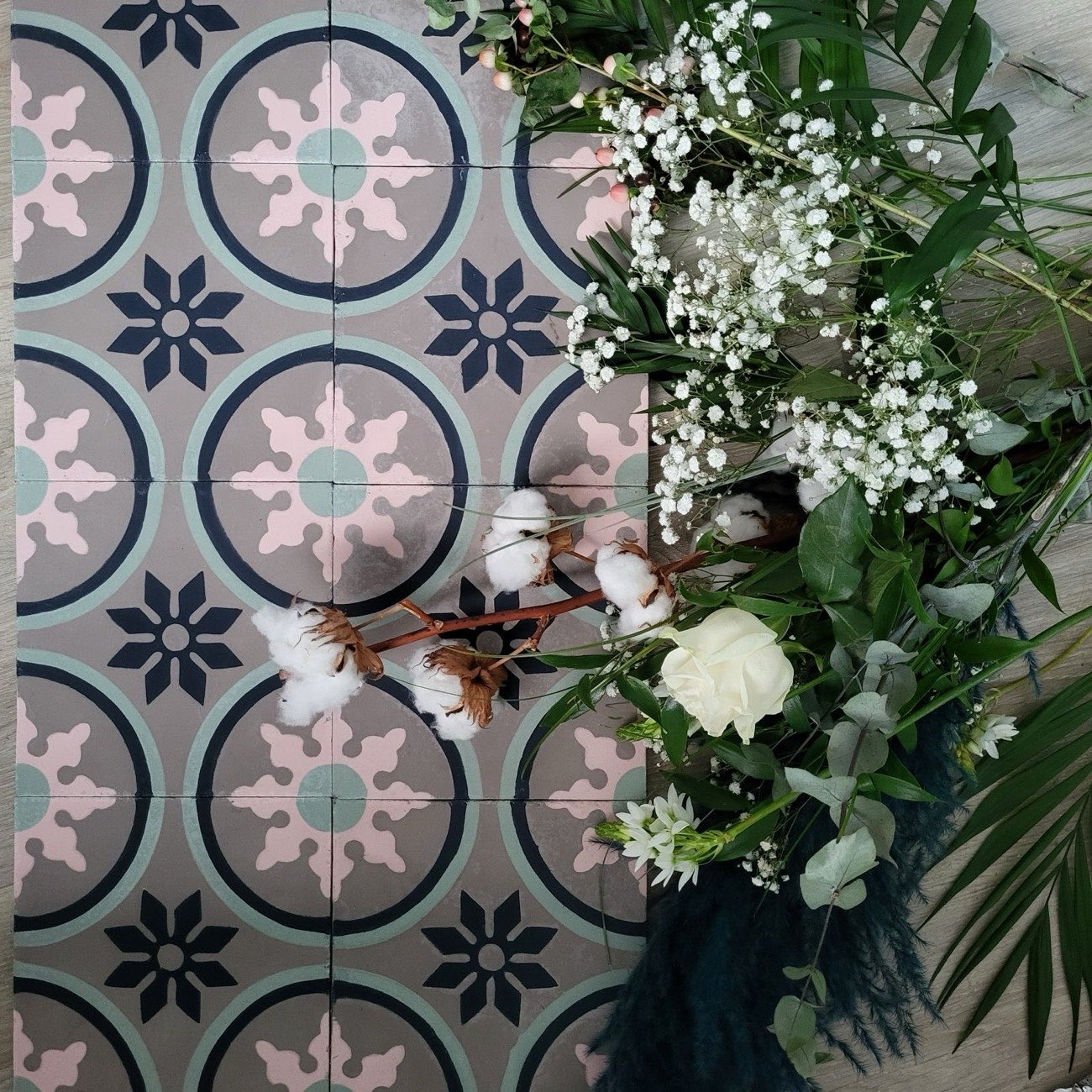 Carreaux de ciment à rosaces roses, vertes et bleu nuit, photographiés avec un bouquet de fleurs